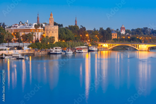 Dodecagonal military watchtower Golden Tower or Torre del Oro and bridge Puente San Telmo during evening blue hour, Seville, Andalusia, Spain © Kavalenkava