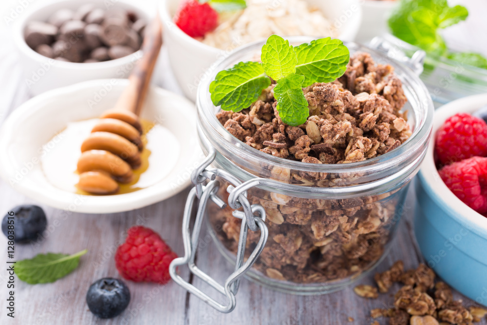 Homemade chocolate granola ingredients, nuts, oats, honey and berries on white wooden background. Healthy brakfast concept.
