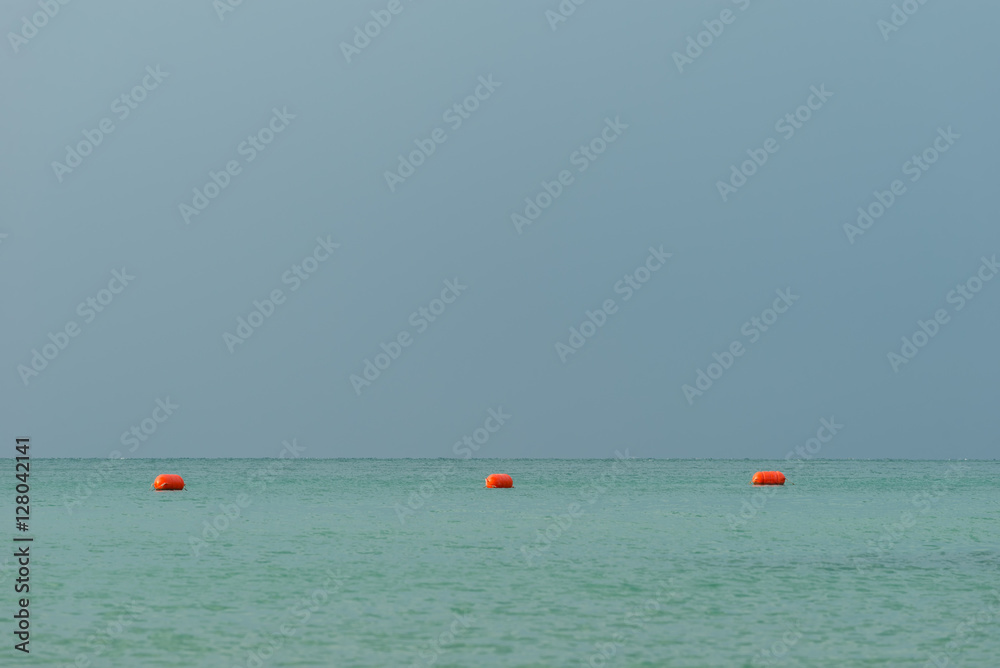Red orange floats, buoy arrangement, make zone in bay, gulf on sea, ocean with blue gray sky in background
