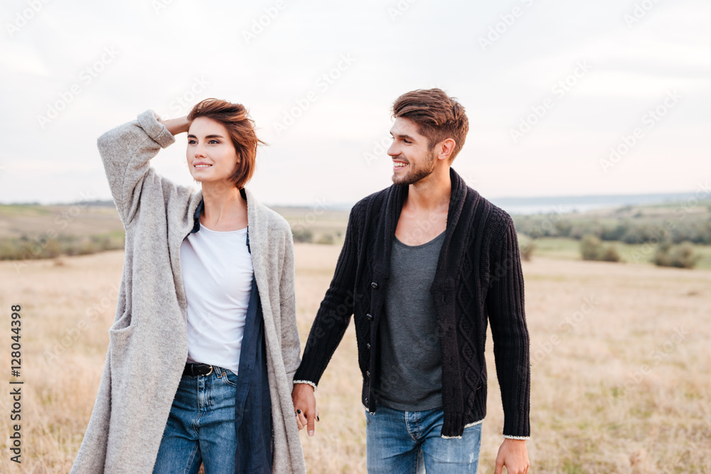 Happy young couple enjoying walk through the grass field