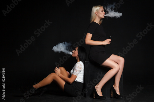 Two beautiful young woman smoking electronic cigarette photo