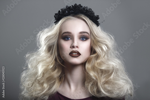 Beauty portrait of a beautiful young blonde woman with gothic make-up and decorative wreath on a gray background.
