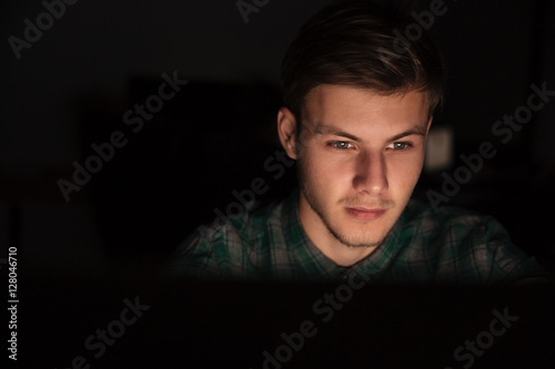 Attractive young man using computer in dark room