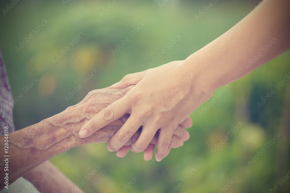 Old and young holding hands on light background, vintage tone.