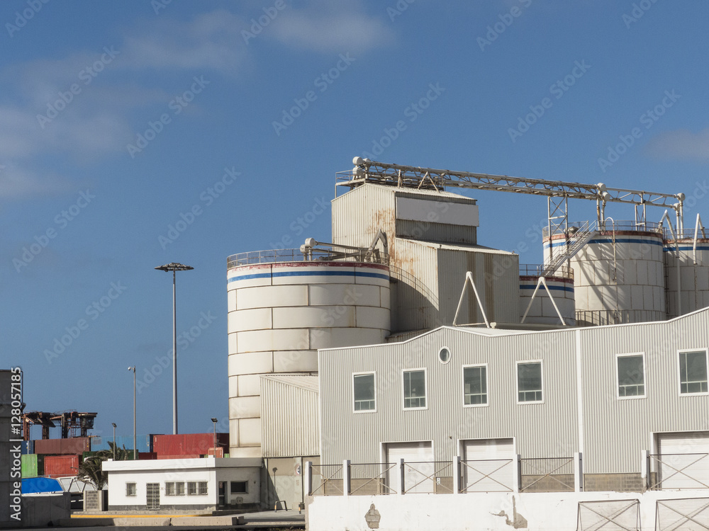 Warehouse with silos on a pier in a harbor at blue sky.