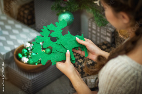 Девушка держит в руках рождественский декор зеленых оленей 