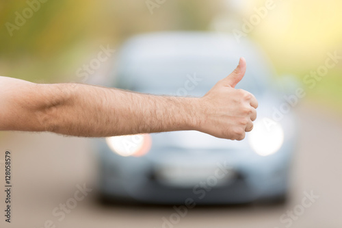 Close up of male hand hitchhiking, asking a coming car for a ride on summer street