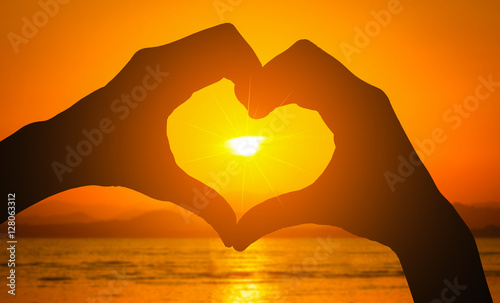 Silhouettes hand heart shaped with sunset and sea