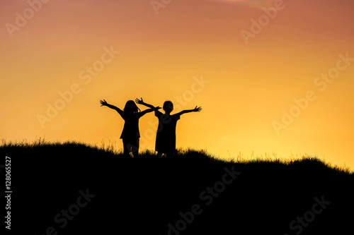 silhouette children standing raised hands up on sunset.