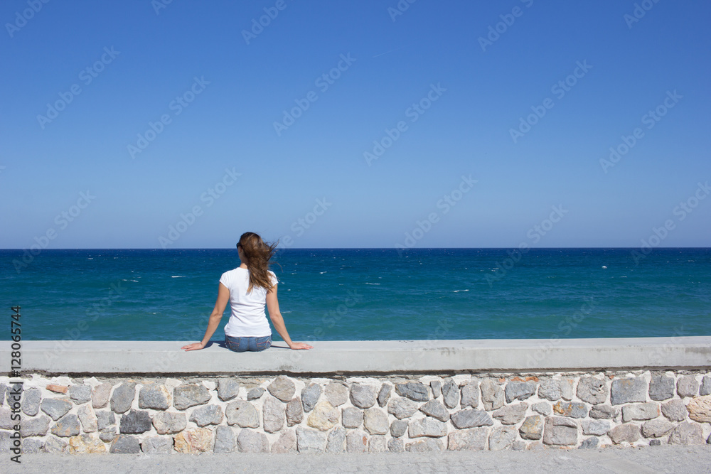 Young woman sitting on embankment and looking to the horizont. Crete, Greece