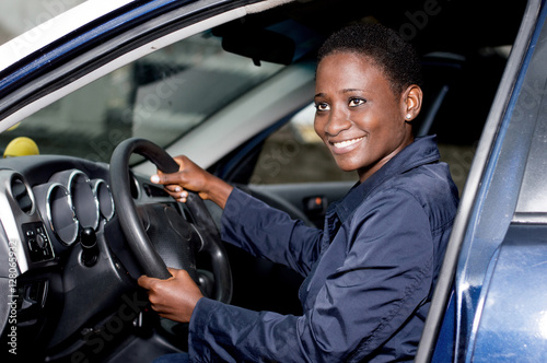 Young woman sitting in a car, hands on the steering wheel smiling at the camera