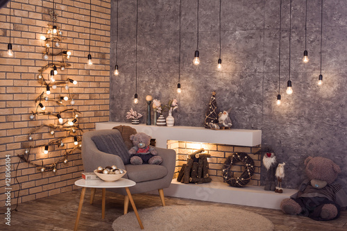 Creative wooden Christmas tree at the brick wall of Loft style room with burning bulbs garland and modern fireplace. Scandinavian winter interior of room. Horizontal