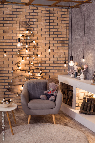 Contemporary interior of living room. Christmas tree, modern fireplace and large gray armchair in loft interior design apartment.