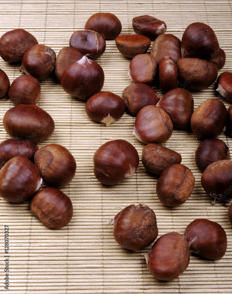 Fototapeta premium raw chestnuts on bamboo napkin over orange wooden background