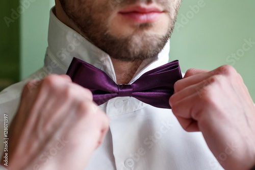 The groom in a white shirt fixing his bow tie
