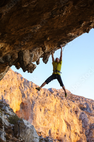 Male rock climber hanging on roof of cave while climbing