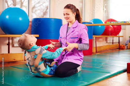 cute kid with disability has musculoskeletal therapy by doing exercises in body fixing belts photo