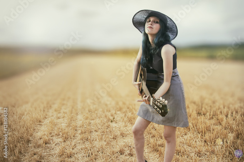 Mujer tocando la guitarra en un campo de verano al atardecer