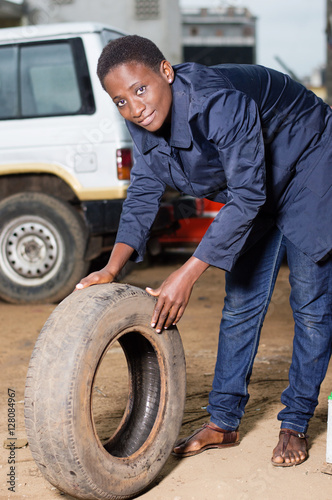 Young woman mechanic with a tire in car workshop