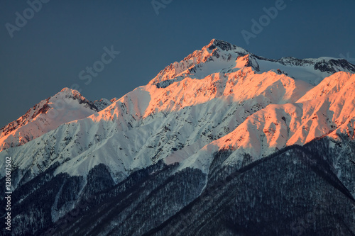 Beautiful mountain scenic winter landscape of the Main Caucasian ridge with snowy peaks on blue sky background at sunset