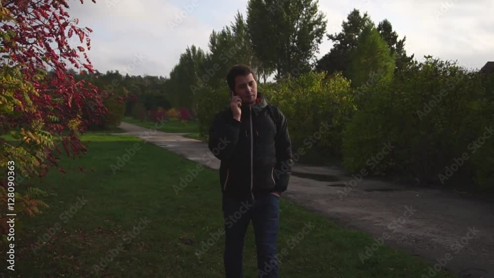 Young man in black jacket walking and talking on the phone in the autumn park slow motion HD Young man in black jacket walking and talking on the phone in the autumn park slow motion HD