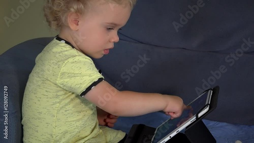 Curious blond kid touching tablet computer screen sitting on couch