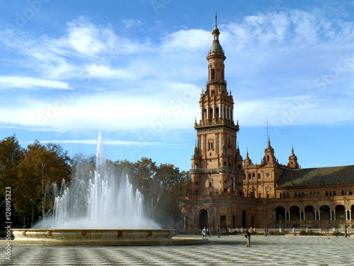 The fountain and the stunning tower of Plaza de Espana under cloudy blue sky, Seville, Spain 