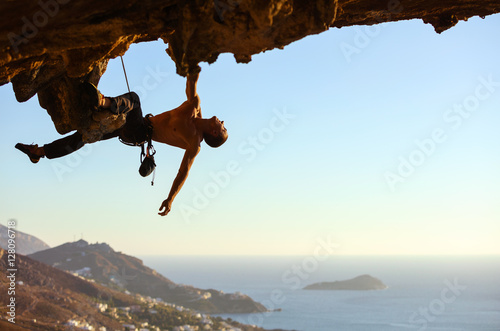 Young man climbing on roof of cave, view of coast below