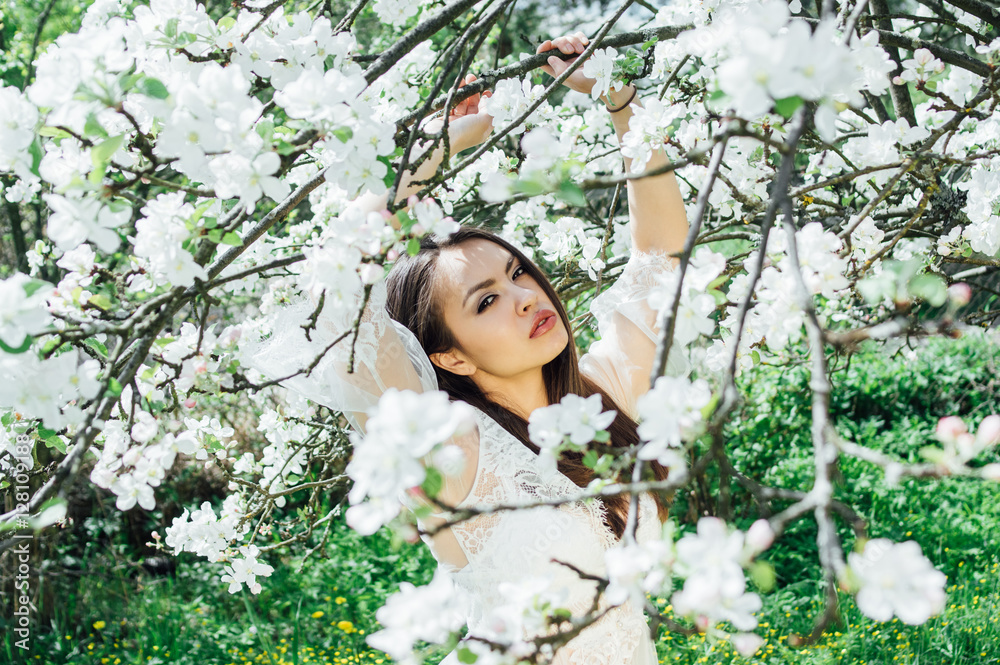 Portrait of young girl in white dress in blossom apple garden, looking to the camera Portrait of young girl in white dress in blossom apple garden, looking to the camera