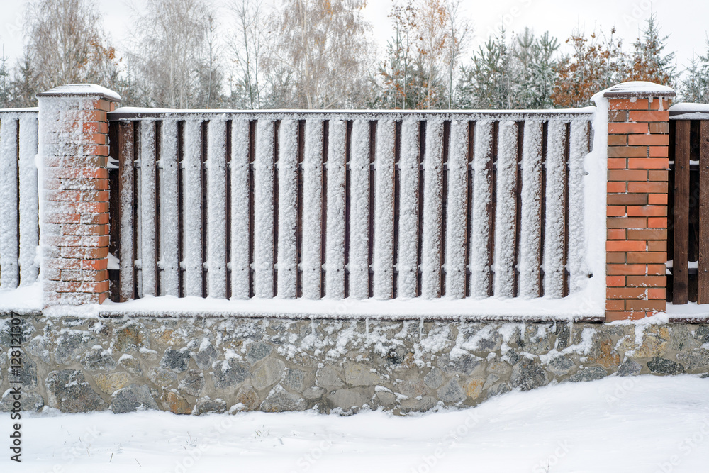 wooden brown fence with brick pillar in snow and frost. wooden brown fence with brick pillar in snow and frost.