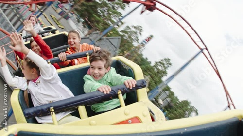 Happy kids yelling, raising arms and waving while riding roller coaster in amusement park photo