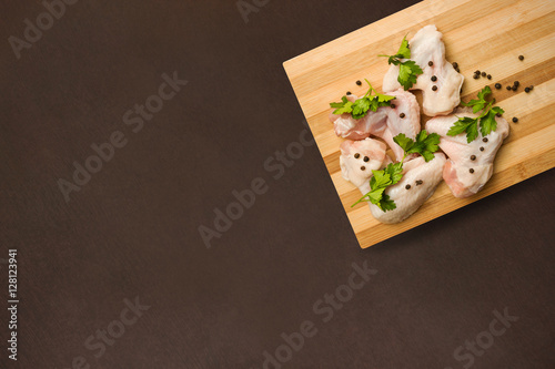 Raw chicken wings with spices on a cutting board and a dark 