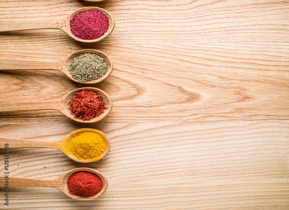 Assortment of colorful spices in the wooden spoons on the wooden