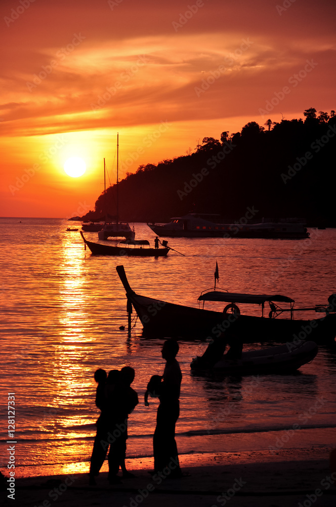 a silhouette of family standing around seashore with boats and sunset sky background a silhouette of family standing around seashore with boats and sunset sky background
