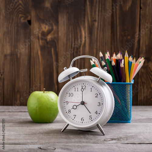 Retro alarm clock with colored pencils and green apple