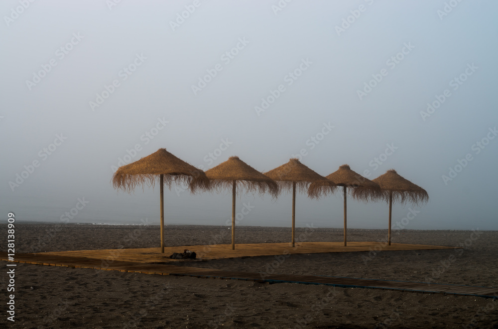 Playa con bruma y sombrillas de paja