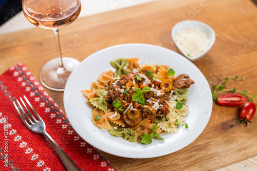 Italian pasta Farfalle with meat, olives, basil and mushrooms. Rose wine glass.