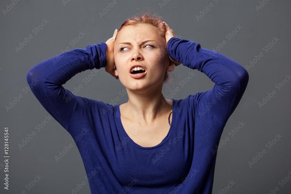 Young woman with headache, hands on the head, painful facial expression, gray background Young woman with headache, hands on the head, painful facial expression, gray background