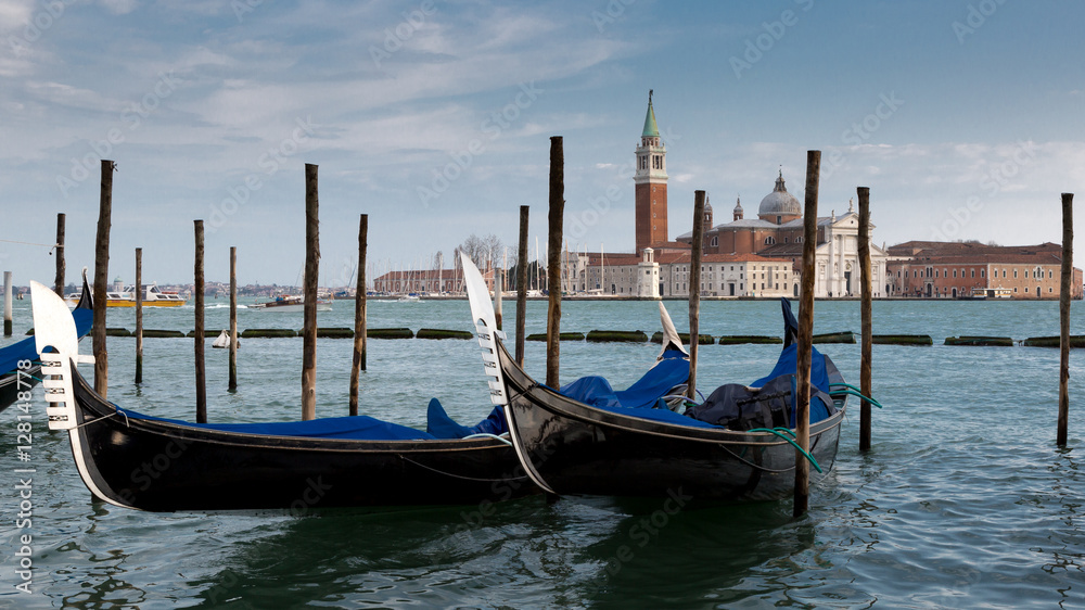 View across the grand Canal in venice with two gondolas in the foreground and blue cloudy sky background.