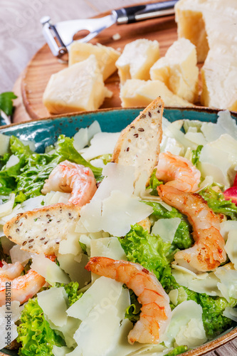 Shrimp salad with parmesan cheese, croutons, tomatoes, mixed greens, lettuce and glass of wine on wooden background. Healthy food. Top view