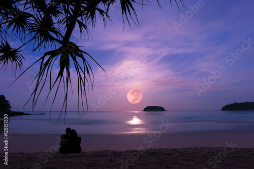 Silhouette of happy couple at luxury fullmoonset  horizon over andaman sea.Couple embracing on the beach enjoying amazing fullmoonset with palm tree in foreground ,Phuket
