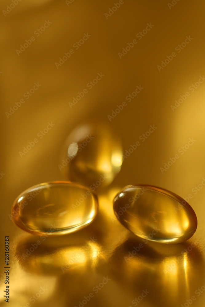three oil capsules on blurred golden background three oil capsules on blurred golden background