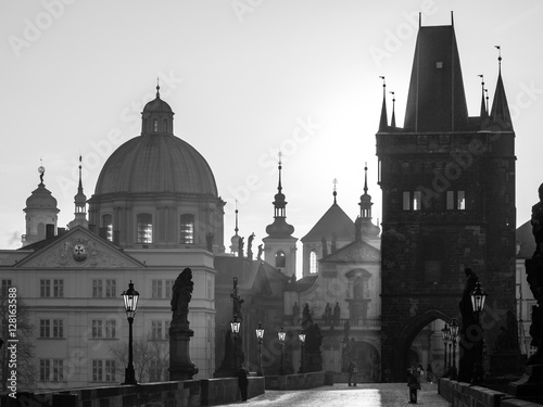 Morning haze on Charles Bridge with towers of Old Town, statues, street lamps and Old Town Bridge Tower, Prague capital city of Czech Republic, Europe. Black and white image.