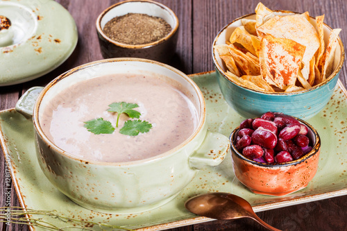 Cream soup with beans, vegetables, herbs and crackers on plate on dark wooden background. Homemade food. Ingredients on table