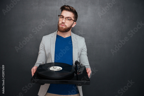 Handsome bearded young man in glasses syanding and holding turntable photo