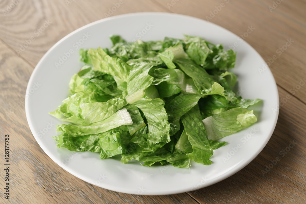 torn romaine lettuce leaves in plate on wood table, diet food