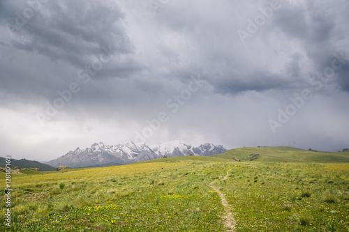 Mountain peaks with snow and green pastures under dark cloudy sky in the At Bashi  Kyrgyzstan