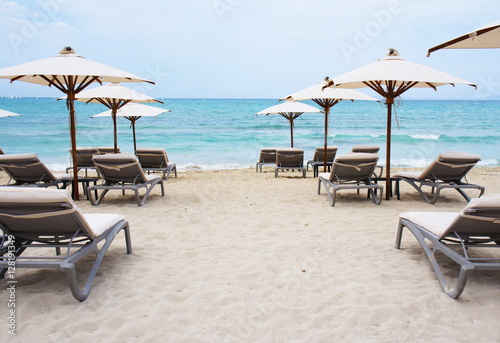 White chaise longue and umbrellas on the empty sandy beach at azure sea Mallorca  Spain