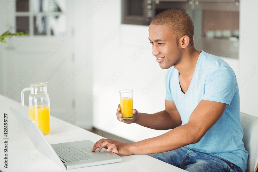 Smiling man using laptop and drinking orange juice Smiling man using laptop and drinking orange juice