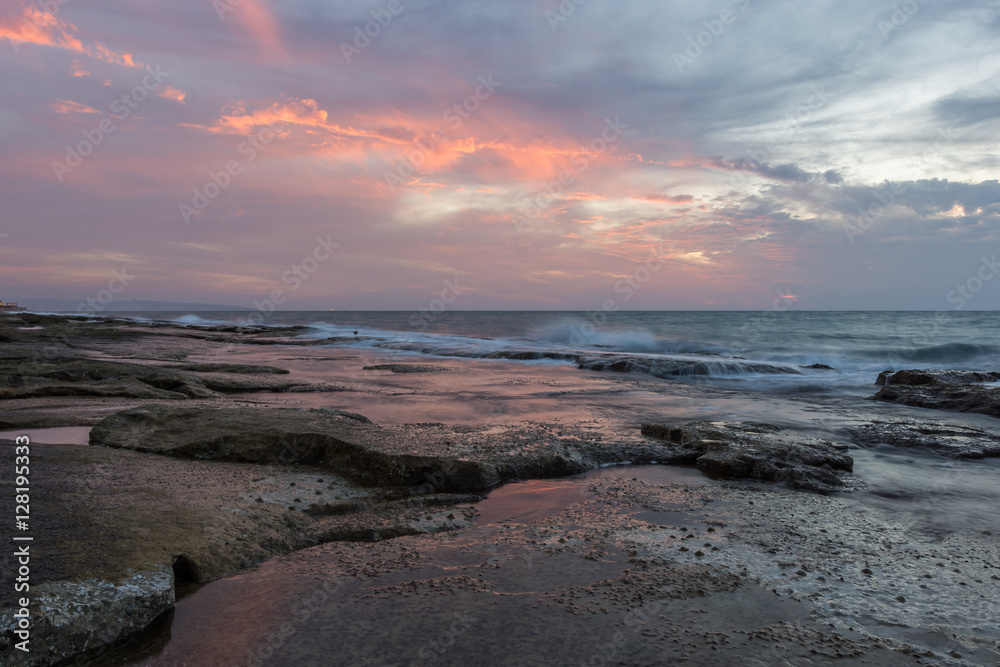 Vivid orange and soft blue sky after sunset over the rocky coastline of western Galilee